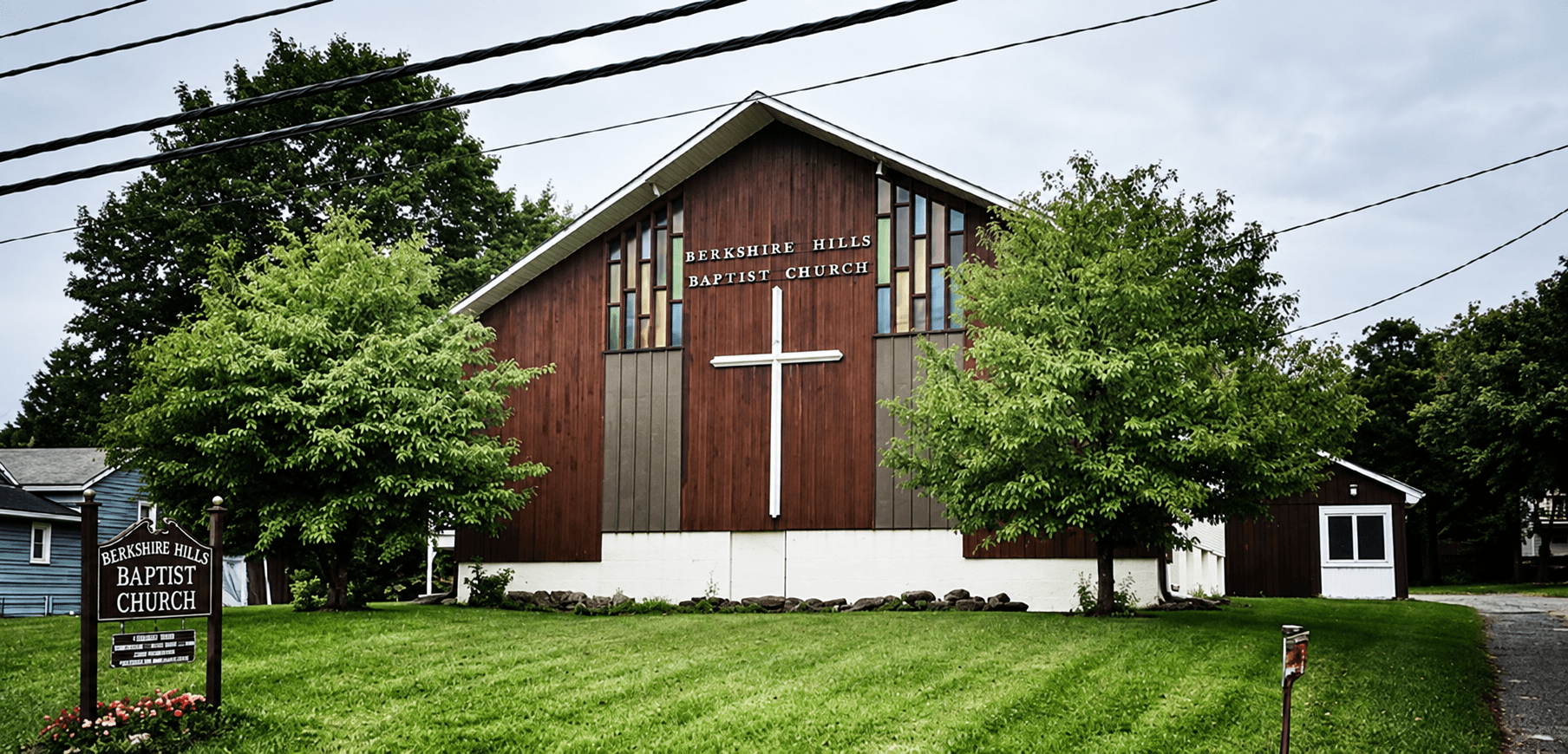 Berkshire Hills Baptist Church in Lee, with its wooden exterior, white cross, and church sign.